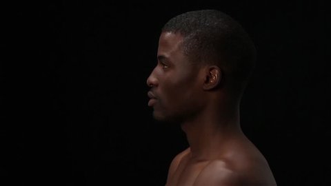 Close up profile of naked black man posing in studio. Handsome model man posing over black background. Man smiling for camera and touching his face. Fashion or vogue concept.