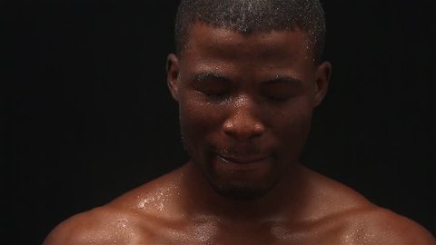 Footage of handsome wet Afro-American man posing for photographer on black background. Professional model looking at camera without any emotions. Afro American man.