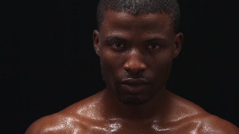 Studio shoot footage of wet Afro-American man posing for photographer on black background. Professional model looking at camera without any emotions. Handsome Afro American man.