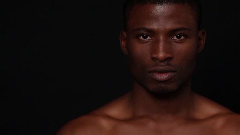 Picture of naked black man posing in studio. Short haired model man with muscular body looking down and up over black background. Fashion or vogue concept.