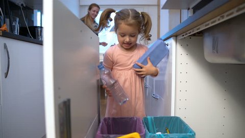 Little girl drops the trash into kitchen recycling bin.