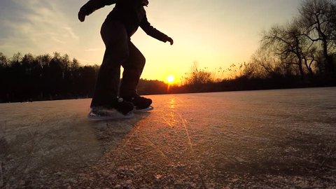 SLOW MOTION, CLOSE UP, LOW ANGLE VIEW: Extreme male ice skater spraying snow when making ice hockey stop on natural frozen lake at beautiful golden sunset on cold winter day before Christmas evening