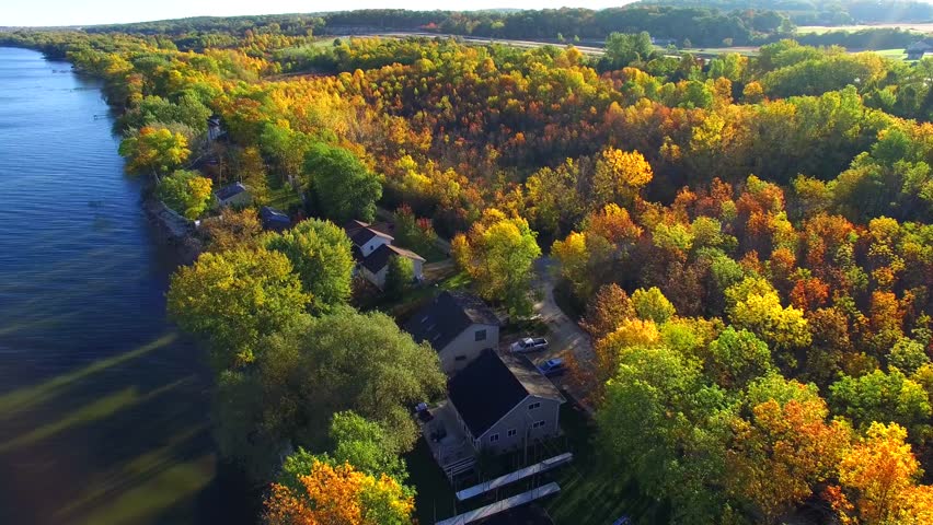 Scenic aerial flight over Autumn trees and homes on rural shoreline.
