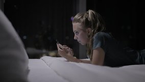 Teenage girl lying on the bed and using her smartphone.