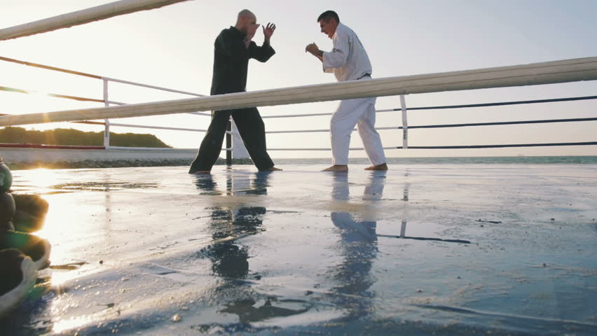 Two professional karate fighters are fighting on the beach boxing ring, slow motion
