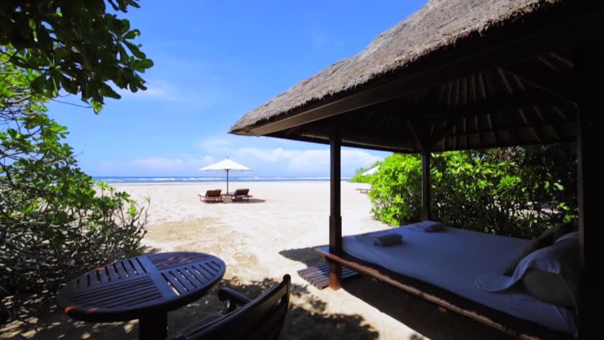 Vacation couple walking and lookin at the distance on beach together in love holding around each other. Beach with umbrellas, deck chairs, beach hut with bad, white sand and Ocean surf. Bali Indonesia