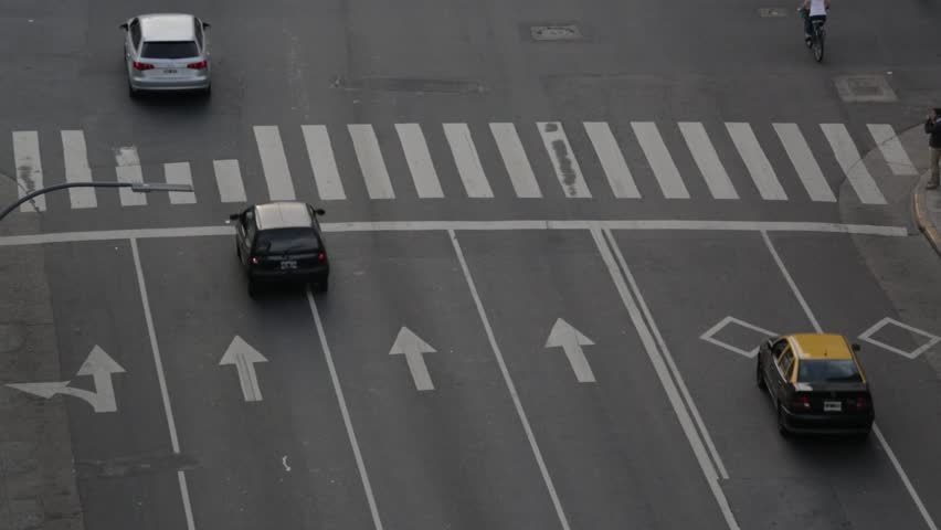 Grey one way avenue with arrows in buenos aires argentina, cars, motorcycles and bikes passing by. Close up scene with telephoto lens from a tall building.