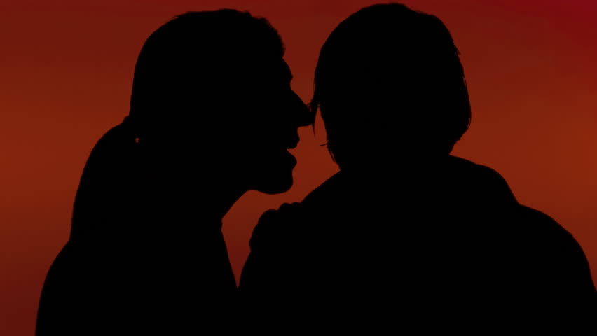 A woman whispering a secret in the ear of a man. Silhouette shot, red background.
 | Shutterstock HD Video #20485426