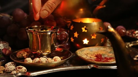 Female hands with beautiful oriental accessories Making Saffron Masala milk Tea with spices. Traditional Moroccan Sweets on Tray. Gala dinner by candlelight. Arab, Turkish, Persian and Indian dishes