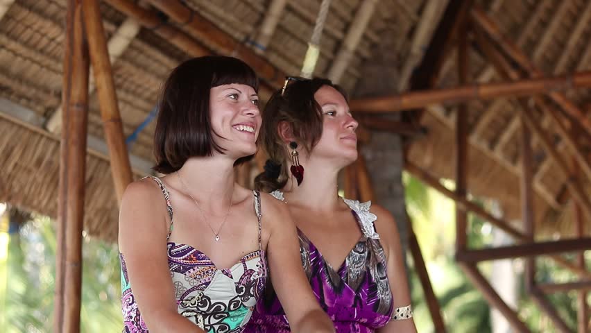 Close up portrait of two beautiful seductive young women sitting near tropical beach of Bali island, Indonesia. Asian vacations, happy time, beautiful view. Talking and laughing.