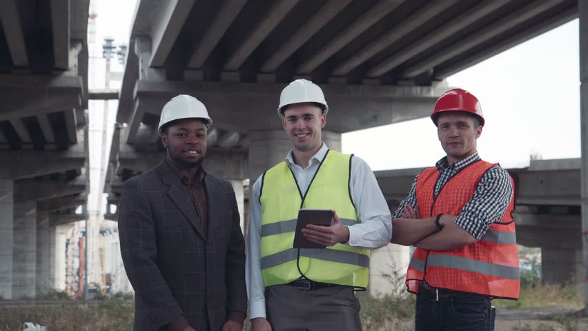 4K shot of front view of three architects one african and two caucasians in protective helmets hard hats looking at camera. | Shutterstock HD Video #20494696