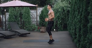 Young  beautiful athlete doing exercise with jumps and swings hands in home garden. Video in 4k slow motion.