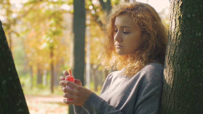 young attractive female blowing soap bubbles in park, portrait, slow motion