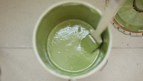 man hand mixes fast green paint in the can on the gray floor