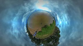 Tiny Little Planet 360 Degree Timelapse. Man, Backpacker is Walking by Lake Bank. Grass is Swaying at the Wind. Tourist is Traveling in Warm Autumn Day. Green Lawn, Blue Cloudy Sky. Fresh Green Trees