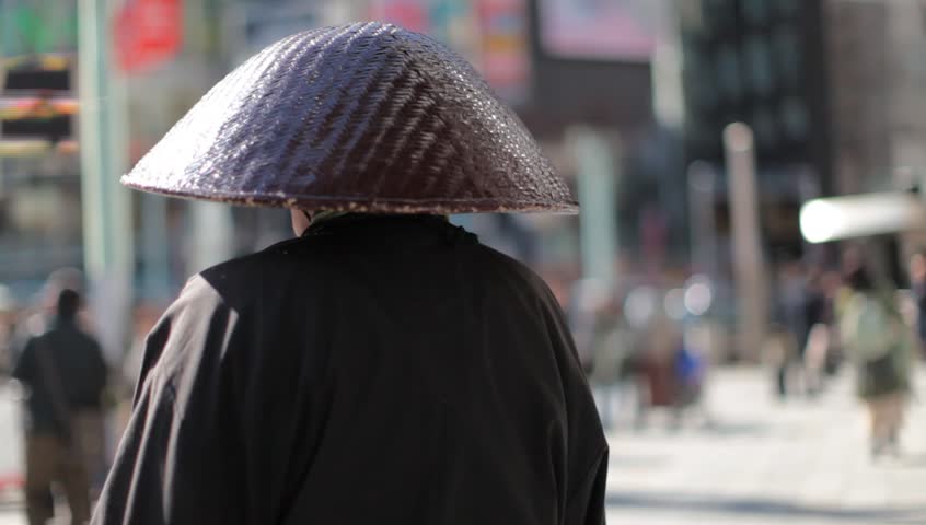 Unidentified monk from behind praying in a busy shopping district with blurred out pedestrians in Tokyo, Japan