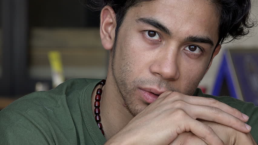 Thoughtful guy waiting for something: frontal portrait sitting at a cafe table