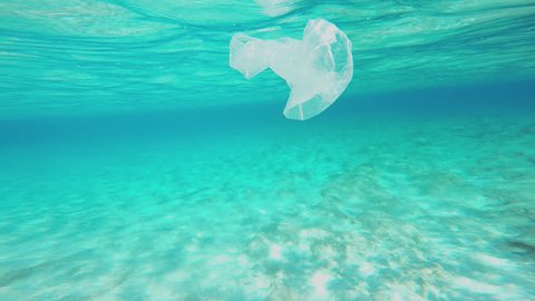 Plastic Pollution Underwater. Camera Is Swimming Around A Plastic Bag Floating Underwater. Tropical, Sunny, Summer, Landscape With A Sun Flooded Sandy Seabed.