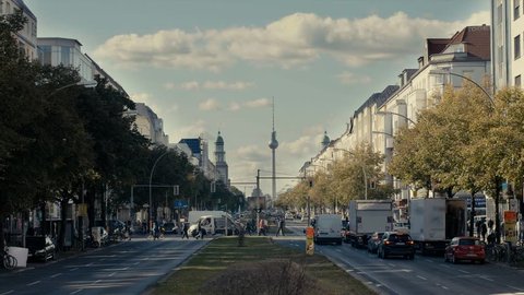 A street in Berlin, with a view of TV tower, many cars, people, moving clouds.