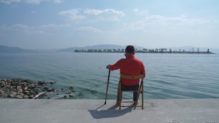 the man with the cane in the red shirt sitting on the chair and enjoys stunning views of the river