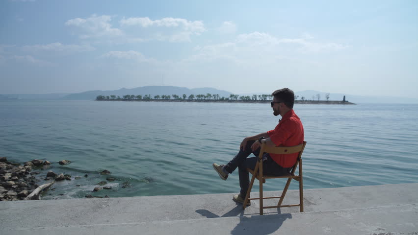 the man in the red shirt sitting on the chair and enjoys views of the river