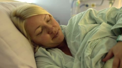 A pregnant woman is lying on her bed and she turns her head when a nurse comes. Close-up shot.