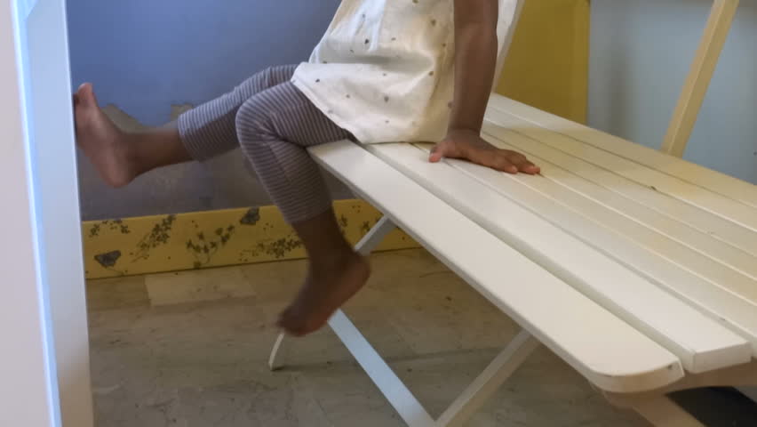 Little girl sitting at the table and moving the legs
