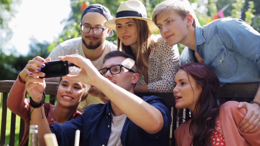 Leisure, party, technology, people and holidays concept - happy friends taking selfie with smartphone and gathering for dinner at summer garden party