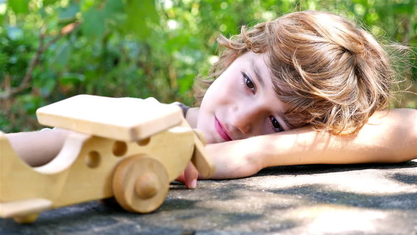 Boy playing with wooden toy airplane on a table outdoors