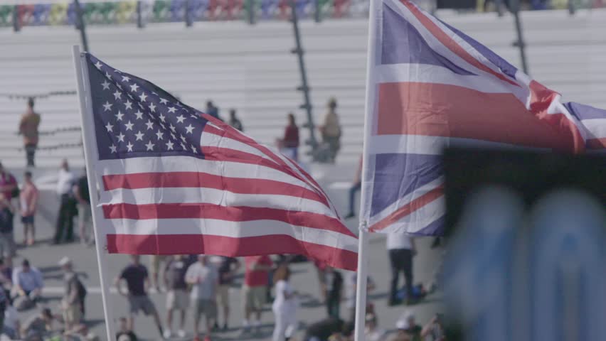 USA and UK Partnership Concept.Slow motion shot of United Kingdom,United States of America Flags Waving in the Wind.Patriotism,Democracy Symbol.Public Event or Parade.Crowds of People in Background.