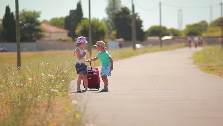 Happy little girl and boy holding hands running  on on the road  with a case
