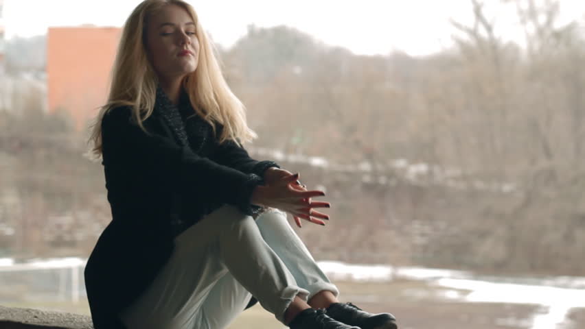 Beautiful blonde young girl fashion look smiling and sitting on parapet