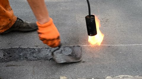 Roofer heating burner flame brushes layer shale coating from the end of the roll of waterproofing to improve adhesion when surfacing next roll. Waterproofing. Flat roof.