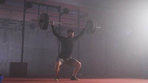 Strong man doing barbell snatch exercise at the gym in slow motion.