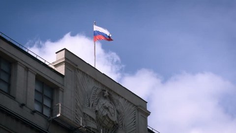 Russian Administrative Concrete Building. Soviet Union Symbols in Front. Russian Federation Tricolor on Top. Facade Decorated With Old Coat of Arms