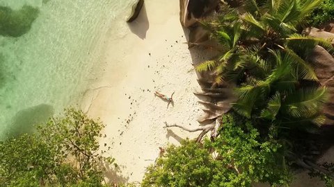 Aerial motion view of Seychelles tropical beach Anse Source D Argent at La Digue island with young woman sunbathing
