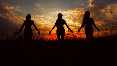 Silhouettes of Three Beautiful Fit Young Female Women Poses Doing Yoga Exercise Outdoors. Photographed Against Red Sunset With Beautiful Sky and Clouds. Concept of Vital Energy, Peace, Unity With