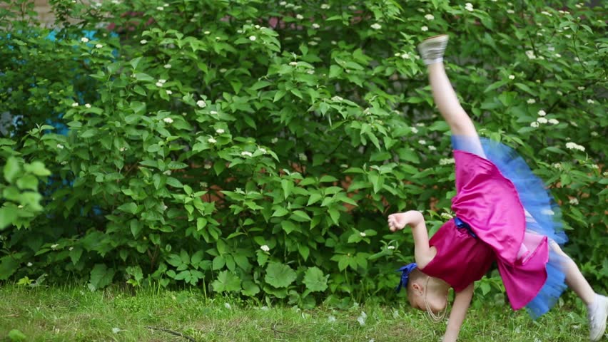 Girl in colored crimson dress doing two cartwheel side on grass near bushes...