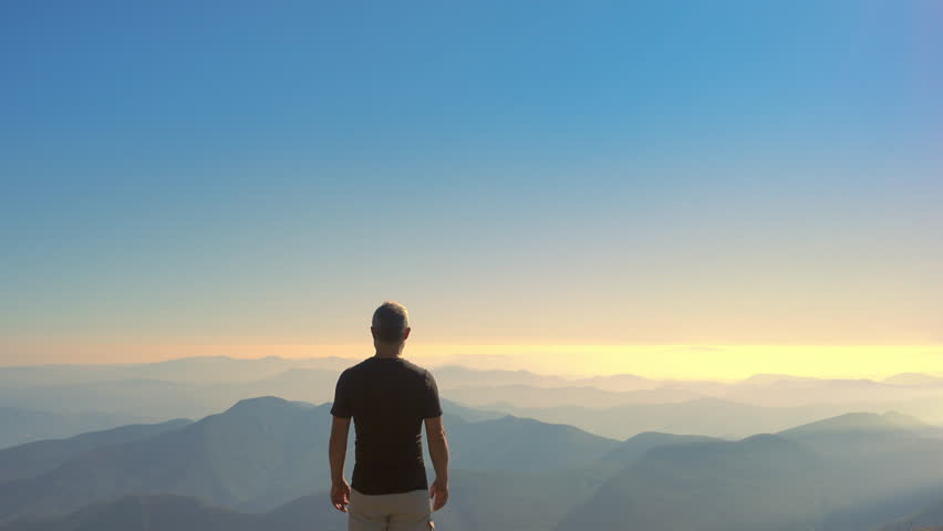 man standing on top of a mountain raising arms to the sky