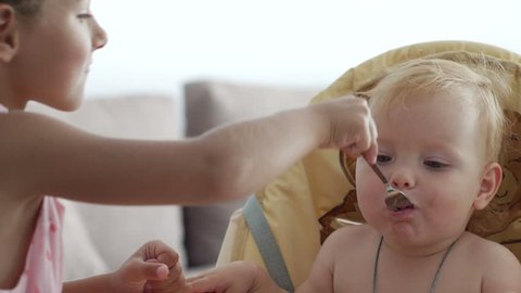 Children eating, little girl is feeding baby in home kitchen