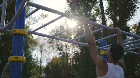 Athletic man doing lifting body on horizontal bar in city park.  Male sportsman performs strength exercises during workout outdoor. Young guy demonstrates static exercise. Training outside Stockvideó