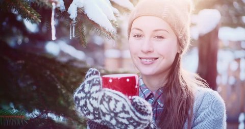 Woman Gives Cup of Hot Tea or Coffee, Enjoying Cozy Snowy Winter Morning Outdoors. 4K DCi SLOW MOTION 120 fps. Beautiful Girl offers Steaming Mug to a Camera by Snow Covered Christmas Tree.