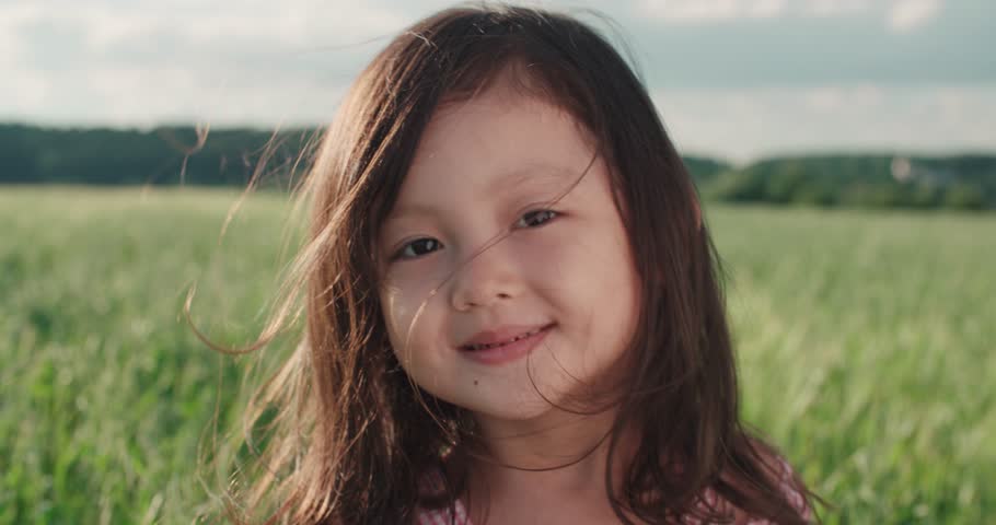 Little Asian girl standing in a green field of young wheat,close-up, flowing hair,slow motion