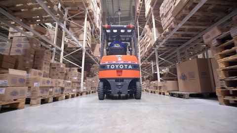 LUBLIN, POLAND - APRIL 21, 2016: Forklift Trucks Move Between Large Metal Shelves at a Modern Warehouse and Unload Pallets with Cardboard Boxes.