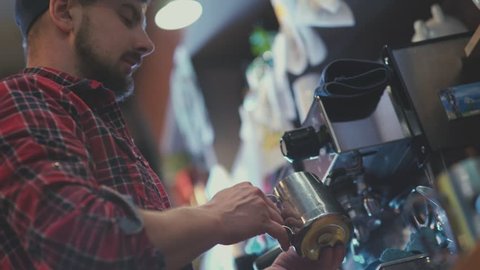 Barista at work. The process of making coffee. A glass of foaming milk. Barista cap and plaid shirt. Barista - nice young man with a beard. Preparing cups of espresso at a busy coffee shop.