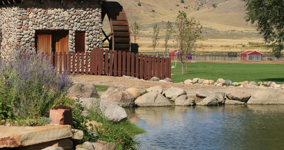 MONA, UTAH - SEP 2016: Water wheel in rural park and garden pond. Park landscape in mountain valley. Lake pond supplies water to decorative waterwheel. water, green grass and mountains in background. 