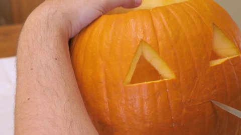Man carves a nose in a pumpkin to make a jack'o'lantern. The shot of the winter squash embodies the spirit of autumn like: Halloween, Thanksgiving, harvest parties and Pumpkin Spice lattes.