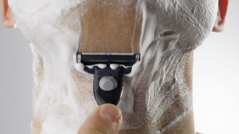 Adult man shaving with foam and manual razer. Close up of man shaving beard.