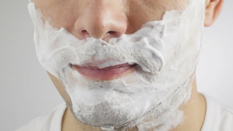 Adult man shaving with foam and manual razer. Close up of man shaving beard.