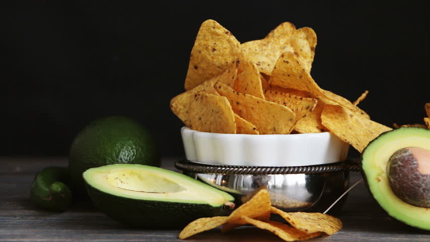 Set of products necessary to cook guacamole sauce - avocado, lime, green chili pepper with chips, nachos. Wooden table, black background, slow pan. Royalty-Free Stock Footage #20667931